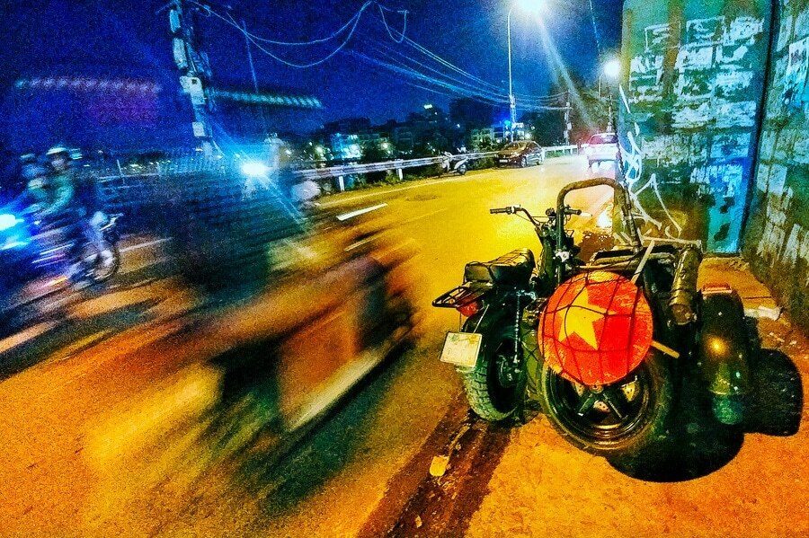 Colour night street photo of a motorbike under neon light with traffic blurred behind it