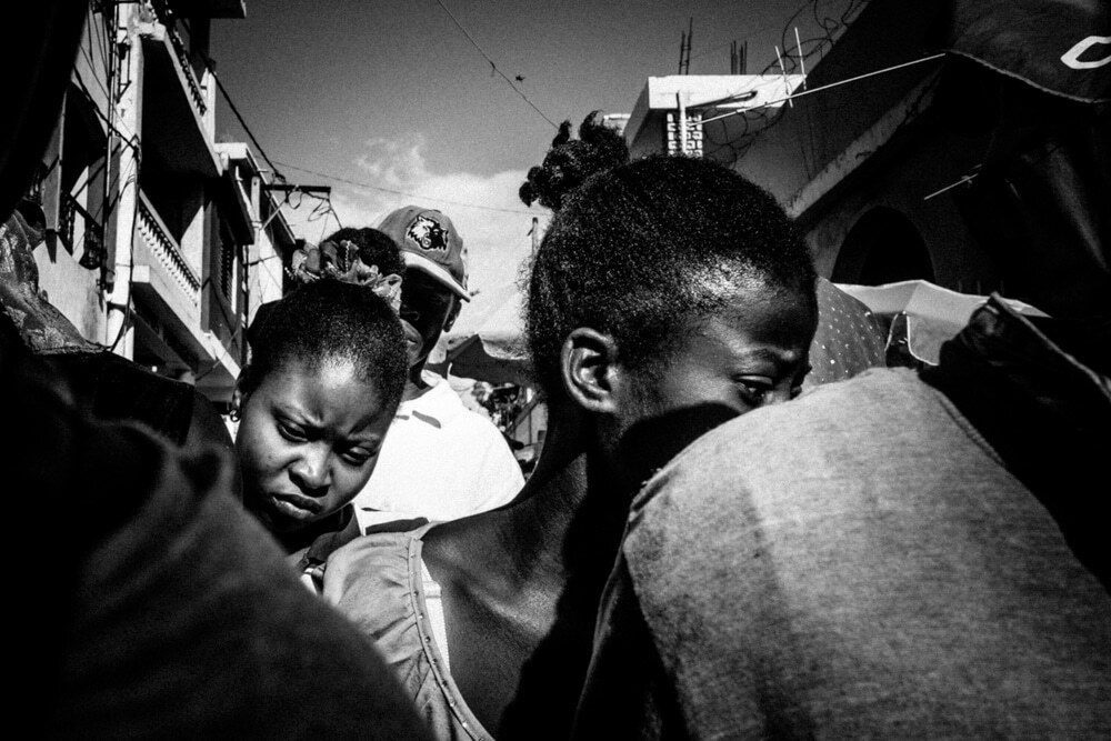 Black and white street photo of a crowd pressed close together, a young woman looking down at the centre