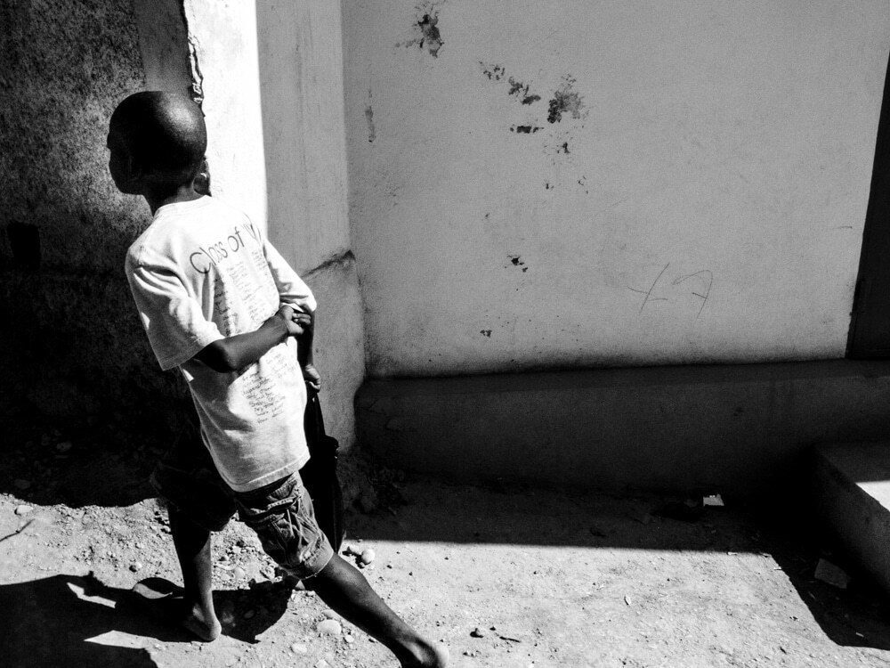 Boy in a white t-shirt walking past a bright wall with a hard black shadow beside him, black and white