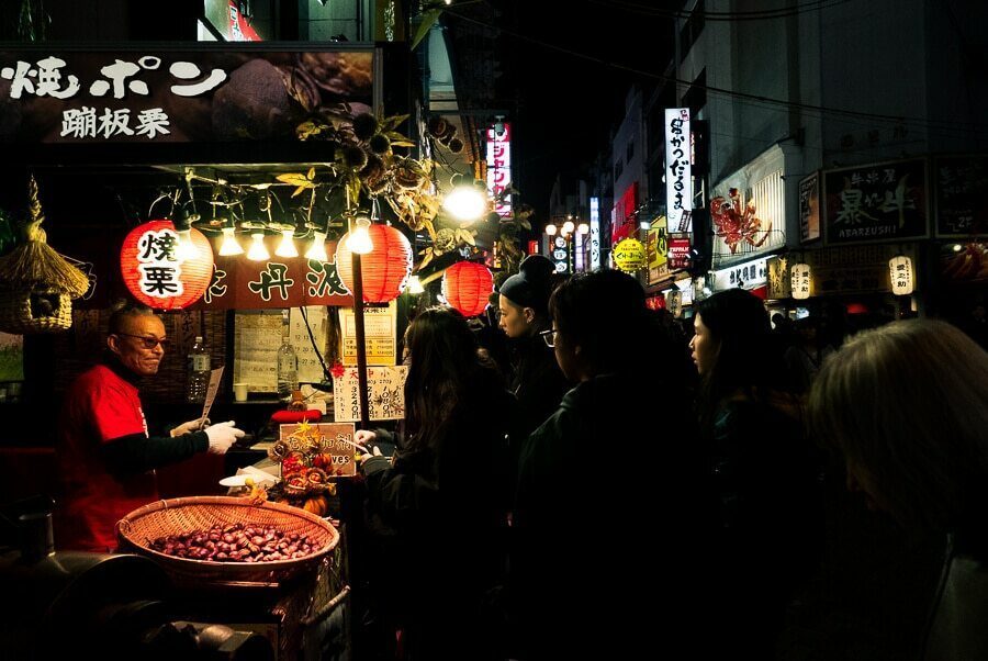 Night street food stall in Japan lit by lanterns with a vendor and customers crowded around