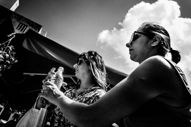 Black and white low angle photo of two women in sunglasses against a bright sky, one behind the other