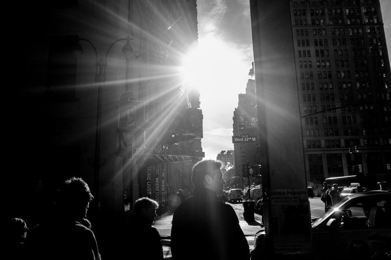 Backlit street scene with the sun bursting between buildings and pedestrians in silhouette