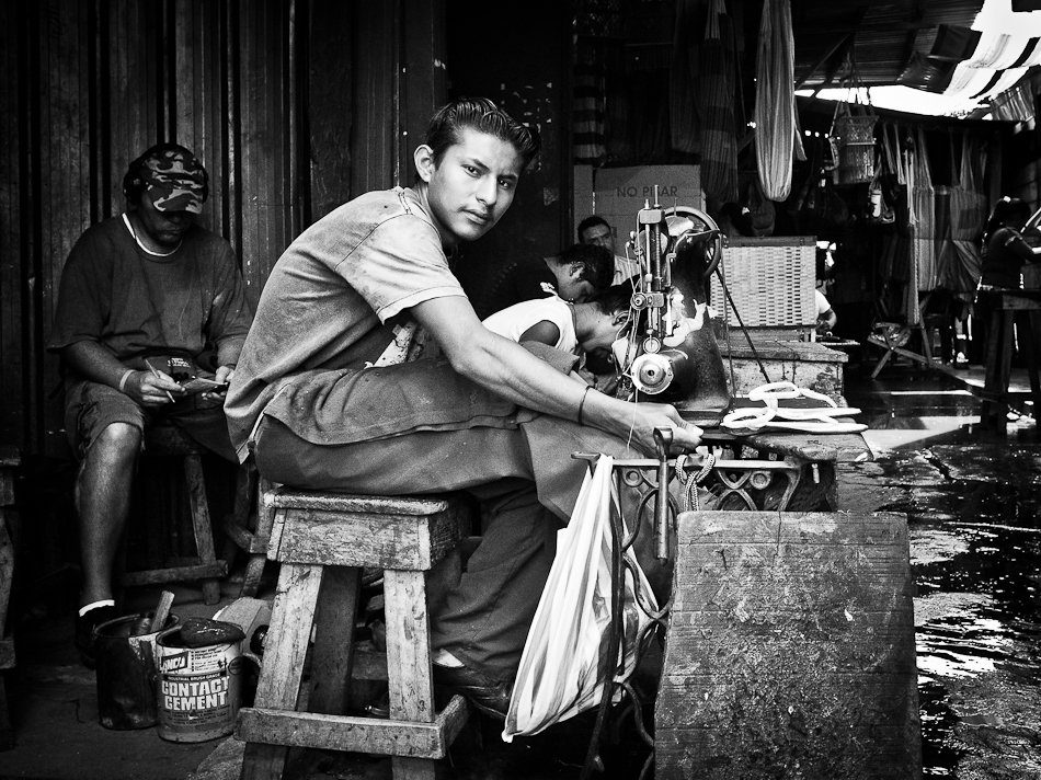 A man sitting on a wooden stool at a street stall in Nicaragua, black and white