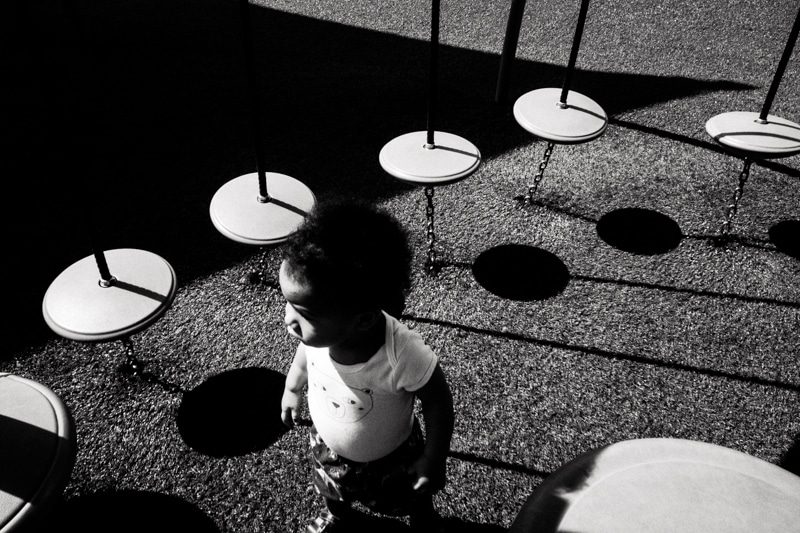 Black and white photo of a small child among round white tables that cast black circular shadows on the ground