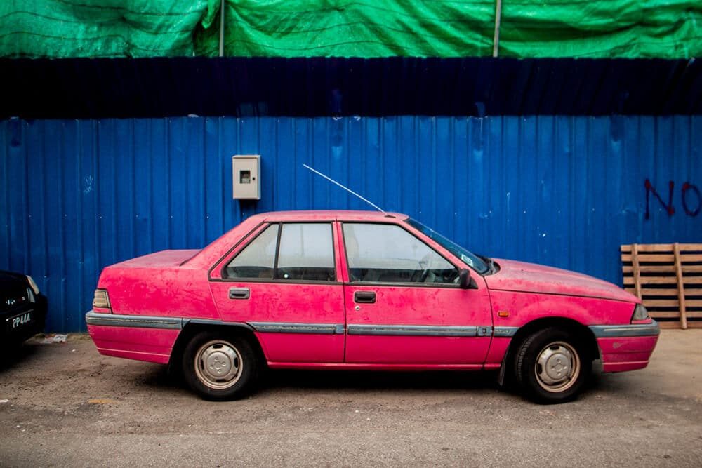 Pink car parked against a bright blue corrugated wall in Penang