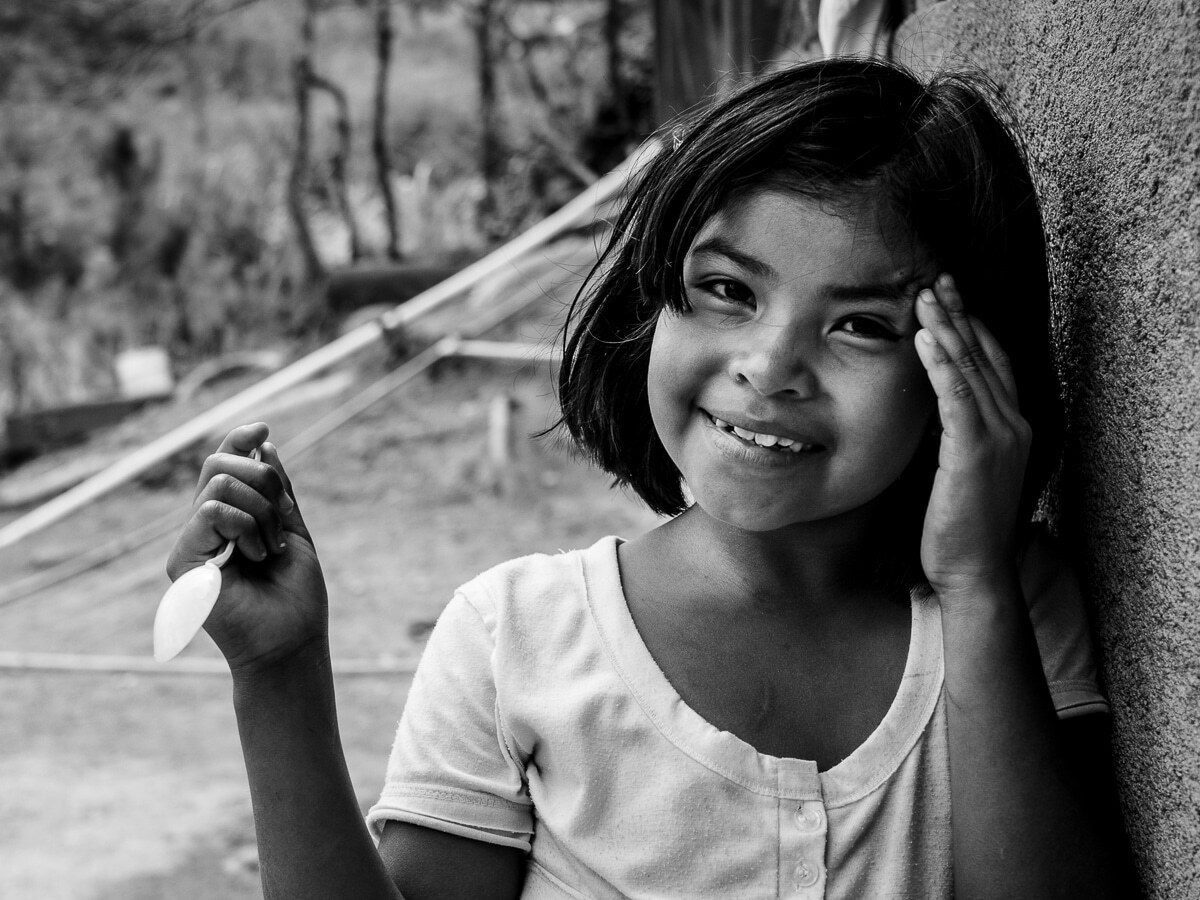 Young girl smiling with her hand on her head, holding a spoon, black and white street portrait
