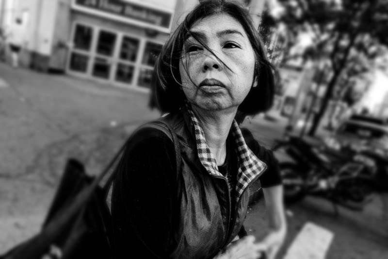 Older woman with windswept hair looking past the camera, black and white street portrait