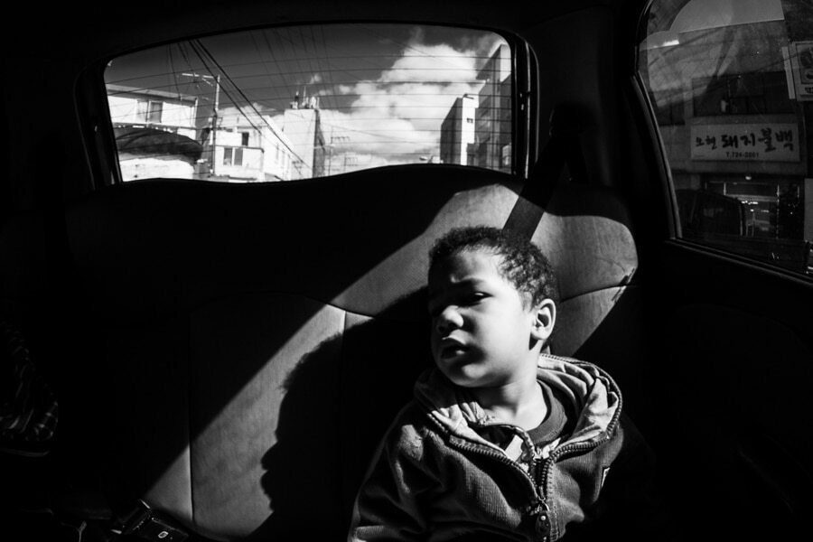 Boy sitting in the back of a car with a strip of hard sunlight across the seat, black and white