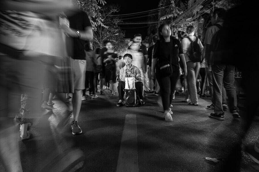 Black and white night street with a crowd walking past as blurred streaks while one child stands out