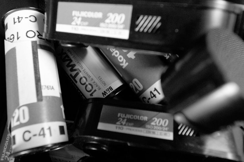 Close-up of a pile of old film canisters, including 120 rolls and 35mm Fujicolor 200 cassettes, in black and white