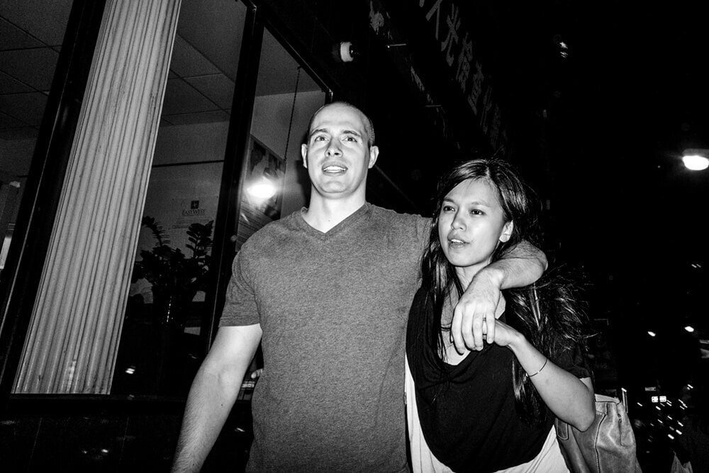 Black and white flash photo of a couple walking arm in arm, both evenly lit