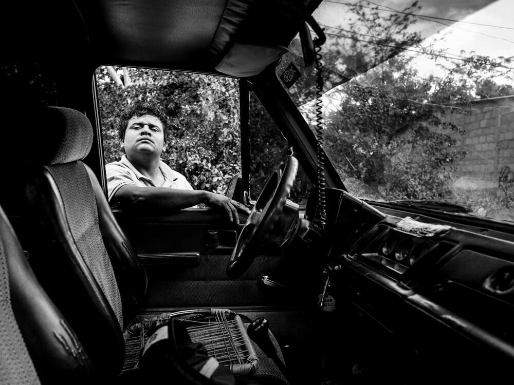 Black and white photo taken from inside a vehicle cab, with a man leaning in the open door window
