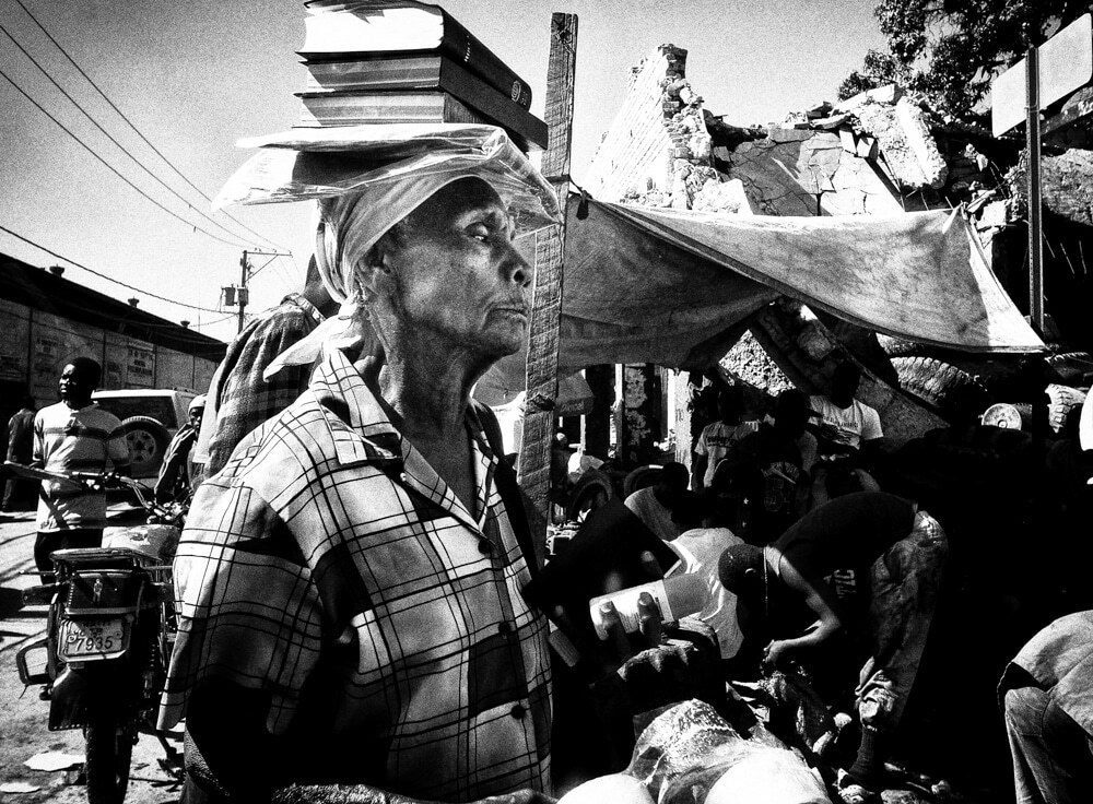 Crowded street market in Haiti with a man in a checked shirt looking up while vendors and loads fill the frame