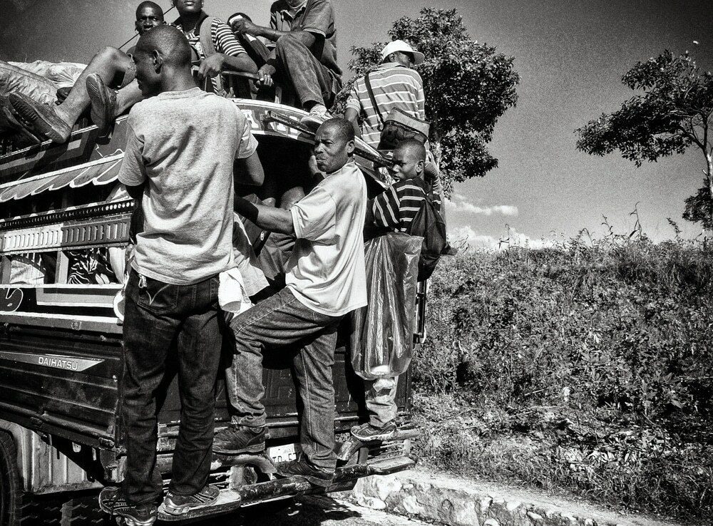 Group of men loading and climbing onto a truck in Haiti, with many arms and faces overlapping