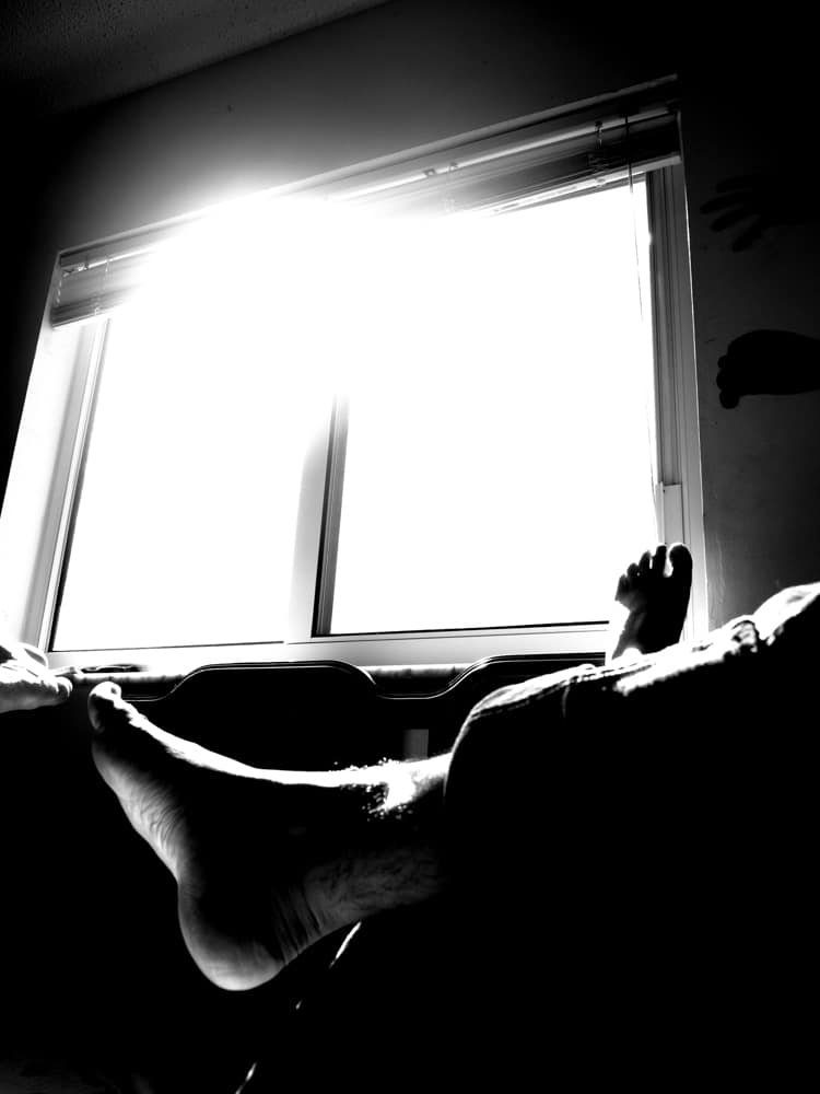 Silhouette of legs and feet against a bright window, high contrast black and white