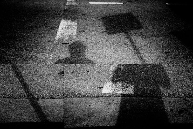 Shadows of a street sign and a person on asphalt with painted road markings, black and white