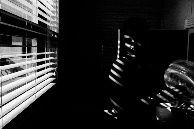 Window blinds casting stripes of light and shadow across a dark room, black and white