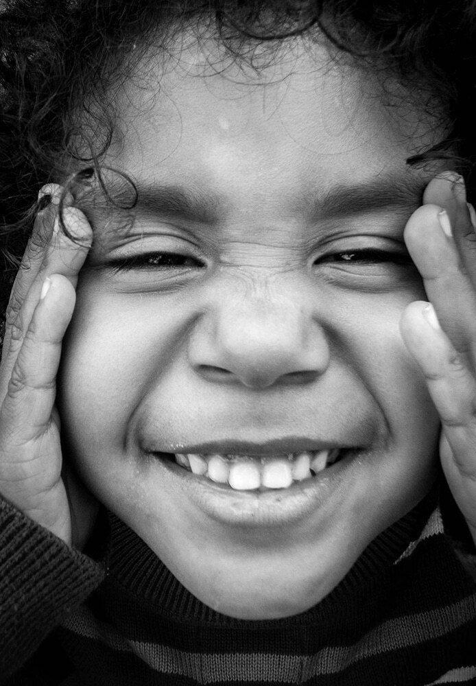 Close black and white portrait of a laughing child pressing both hands against her cheeks