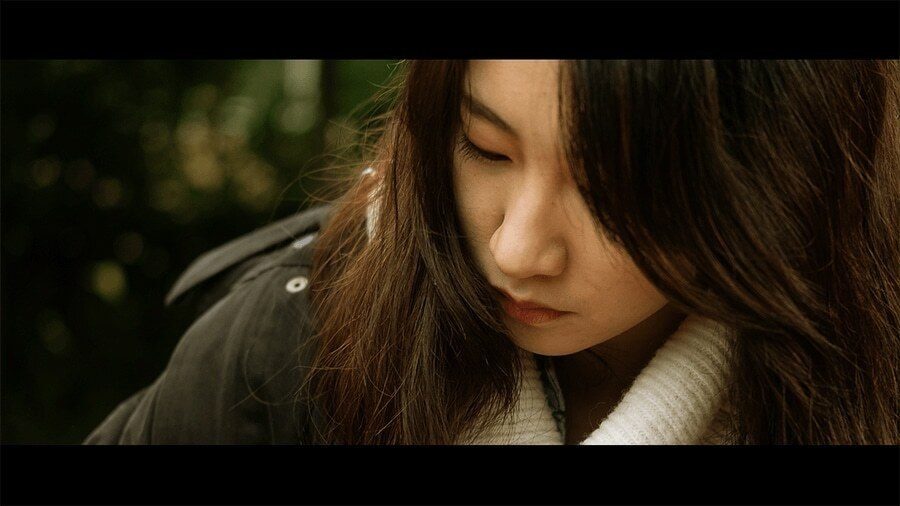 Cinematic color portrait of a young woman looking down, with a soft blurred green background