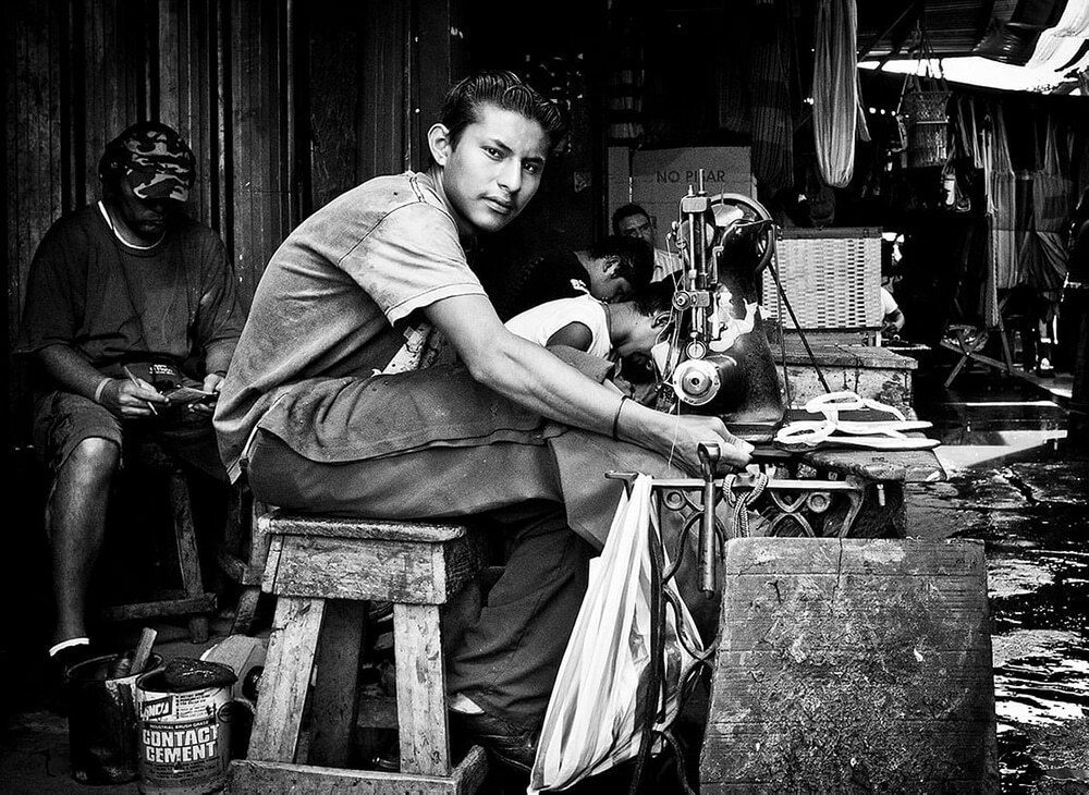 Candid black and white photo of a man working at a street stall, glancing at the camera