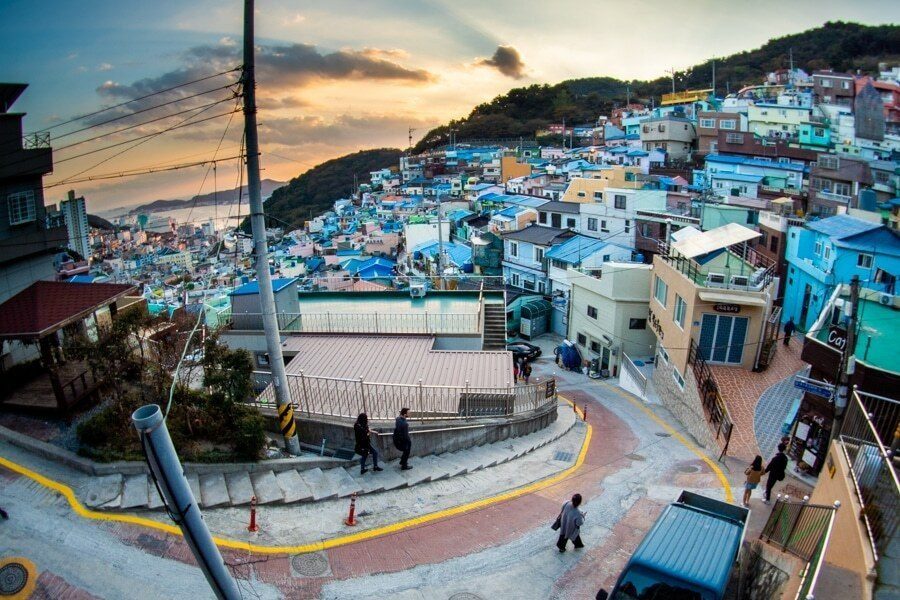 Colorful hillside village in Busan at dusk with a winding road and a few people walking below