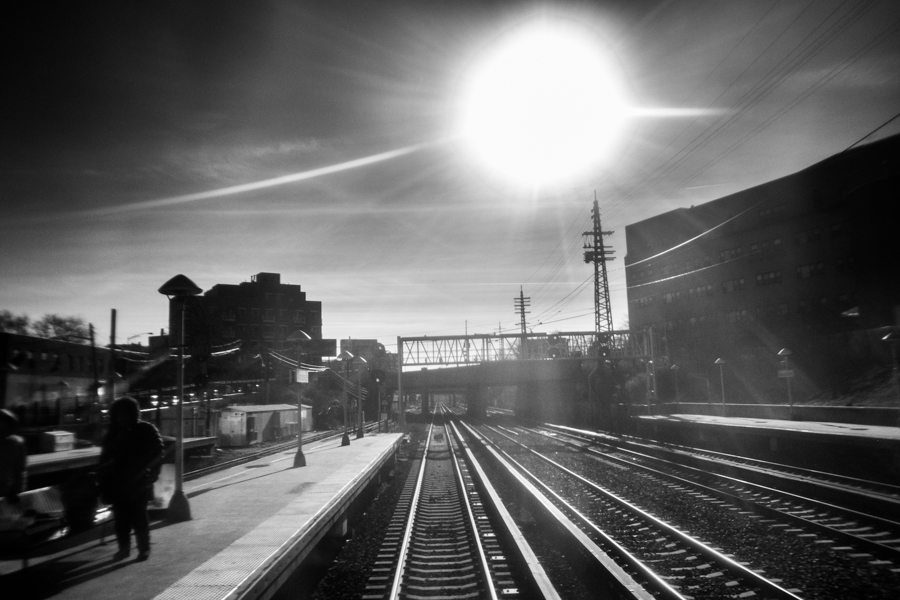 Railway tracks running toward a bright sun with a platform and buildings in silhouette