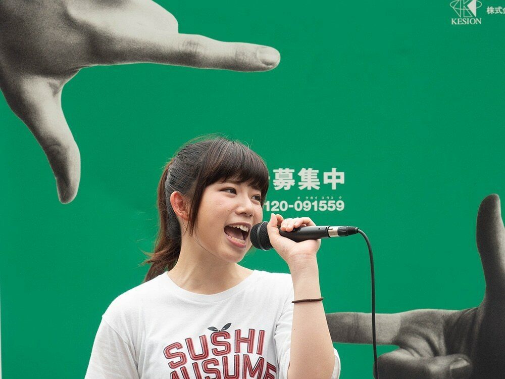 Young singer with a microphone framed between two giant painted hands on a green billboard in Osaka