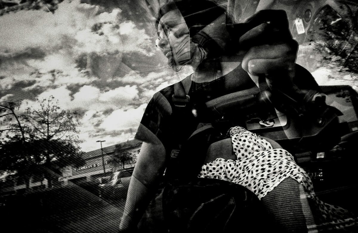 Black and white street photo where a reflection overlays a person's face with a scene outside