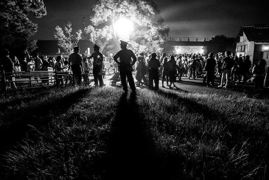 Black and white photo of a crowd backlit by a low sun, with long shadows stretching across the grass toward the camera