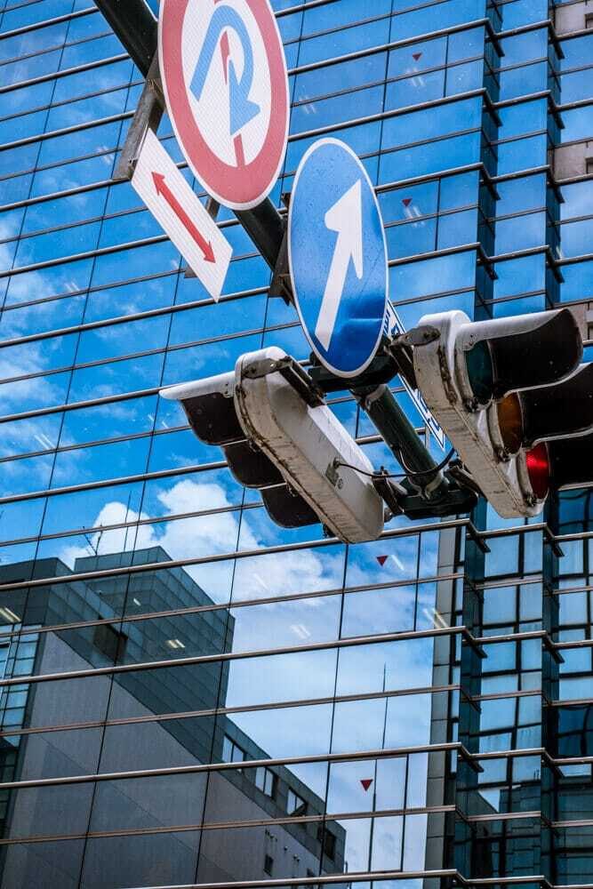 Glass facade of a Kyoto building reflecting blue sky and clouds, with traffic lights and road signs in front