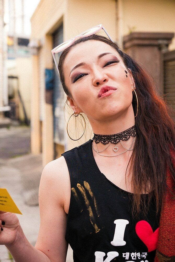 Young woman in an I love Korea tank top making a playful kissing face at the camera on a street in Jeju