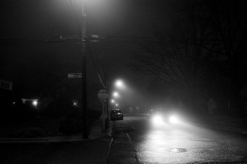 Foggy street at night with blurred headlights and glowing streetlamps