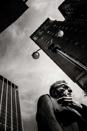 Low angle portrait of a man against a cloudy sky with a streetlamp and buildings at the edges