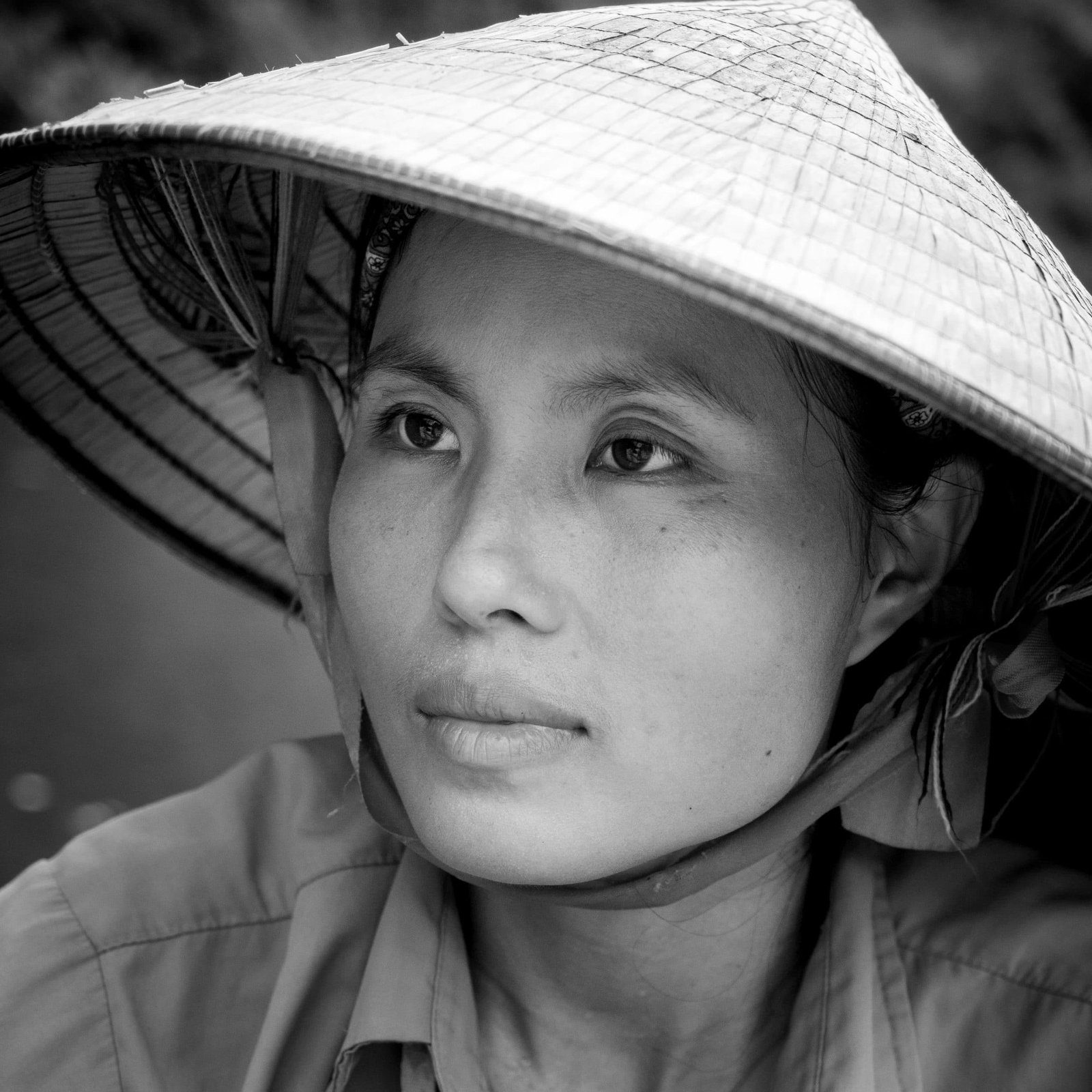 Close-up black and white portrait of a Vietnamese woman in a conical hat looking off to the side