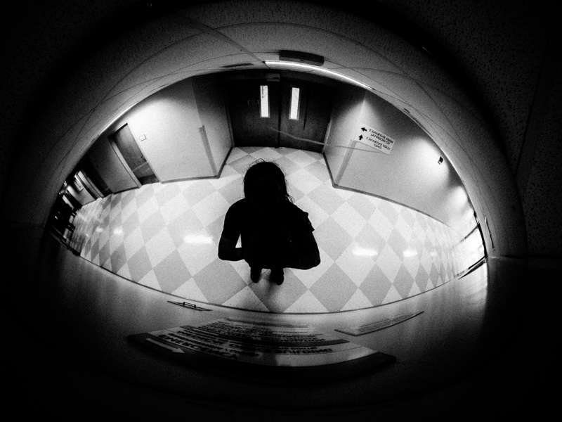 Black and white fisheye photo of a small silhouetted figure standing on a checkered floor at the end of a curved corridor