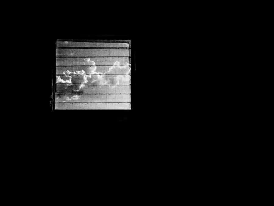Almost completely black frame with a single small window showing bright clouds through horizontal slats