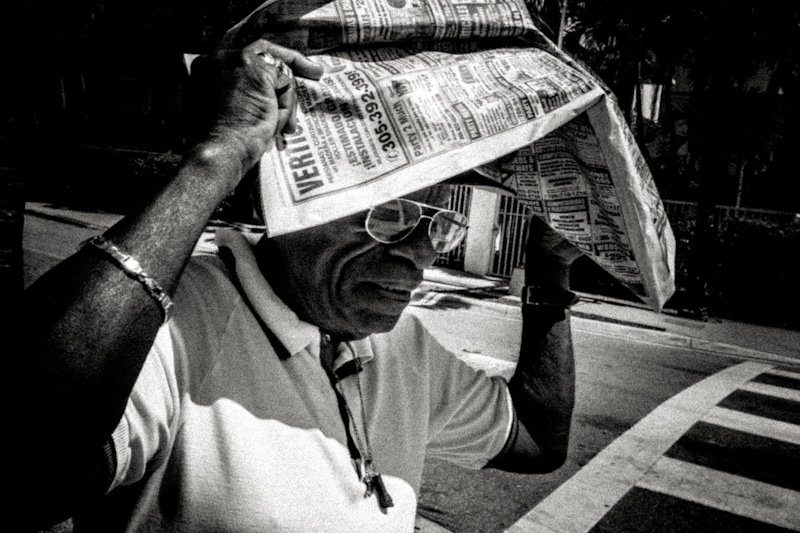 Black and white photo of an older man shielding his head from the sun with a folded newspaper