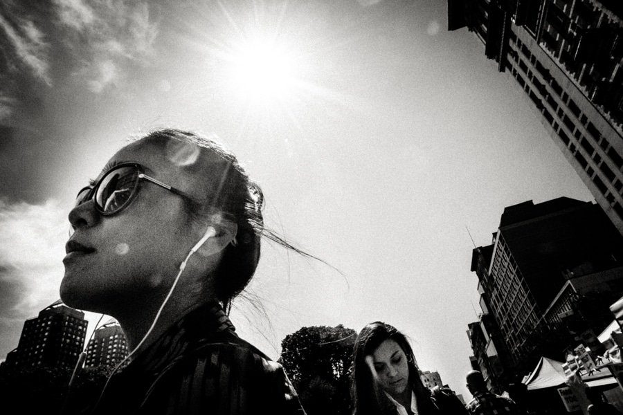 Young woman with earphones looking up into bright sunlight between city buildings, black and white