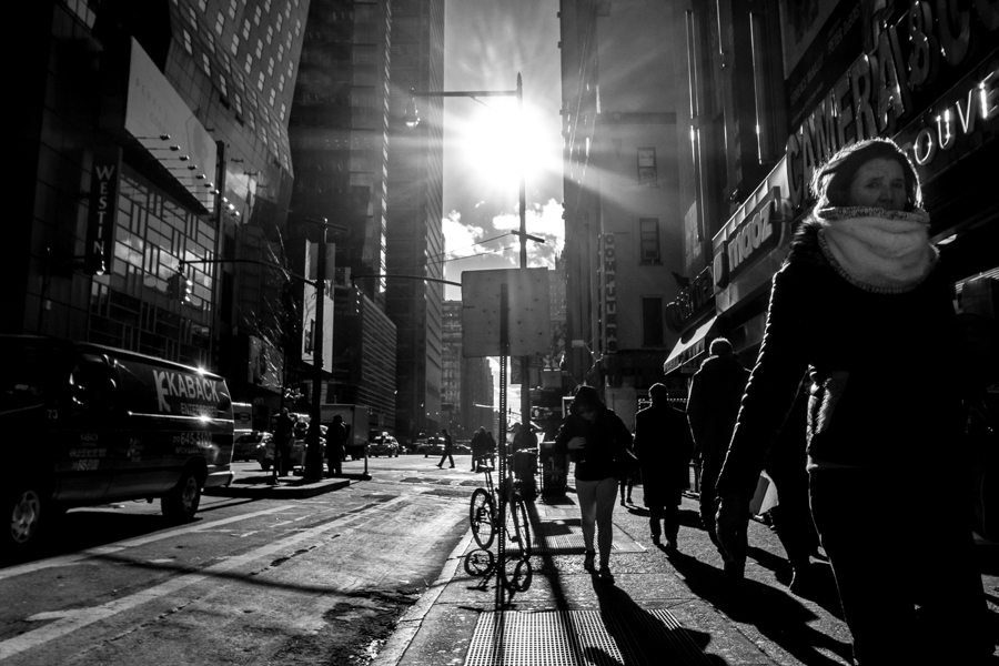 Pedestrians walking on a city sidewalk into bright backlight between tall buildings
