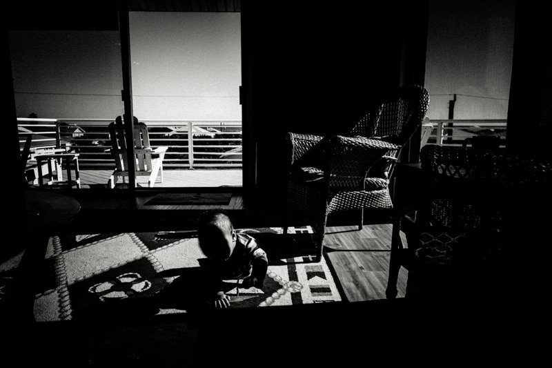 Dark interior looking out through a window onto a sunlit balcony, black and white