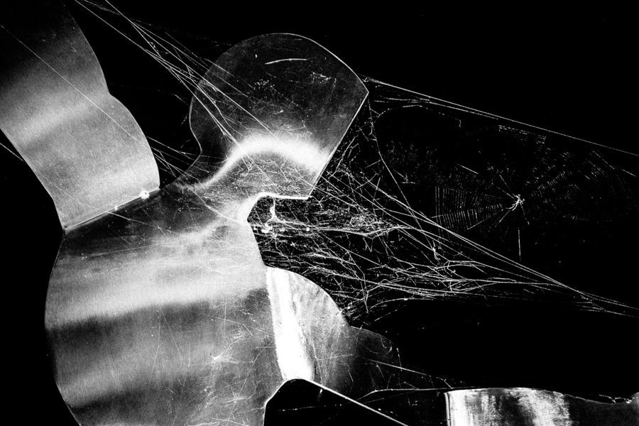 Close black and white detail of rusted metal covered in spider web strands