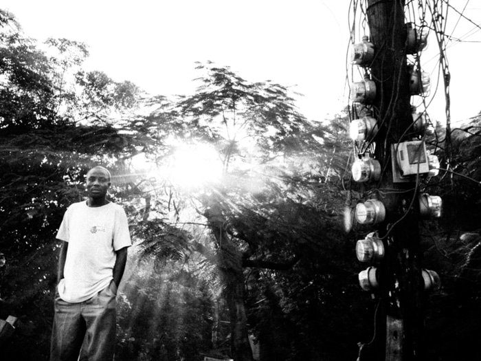Black and white photo of a young man standing in a garden with the sun bursting through trees behind him