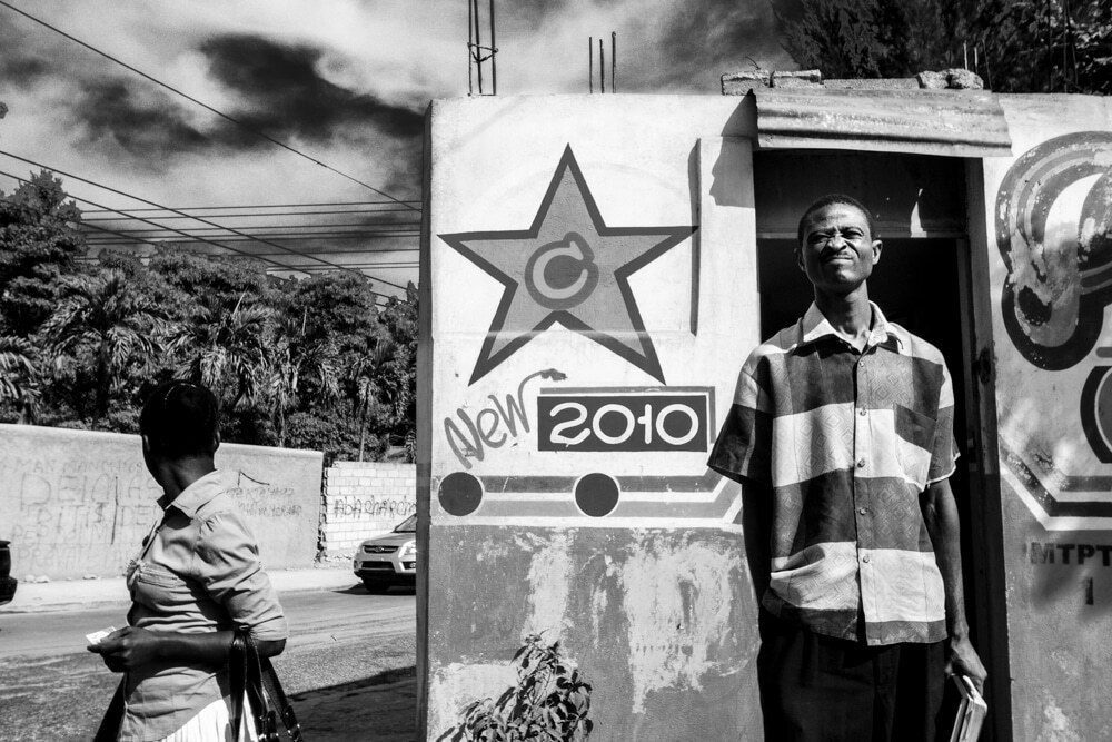 Man in a striped shirt standing in a doorway next to a painted wall with a big star and the number 2010 in Haiti
