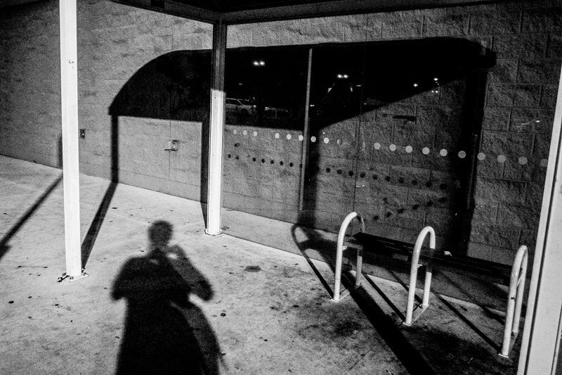 Photographer's own shadow on a sunlit pavement under a bus shelter