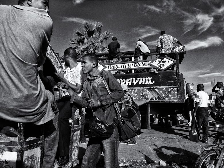 Black and white street photo of people gathered around a painted tap-tap bus in Haiti