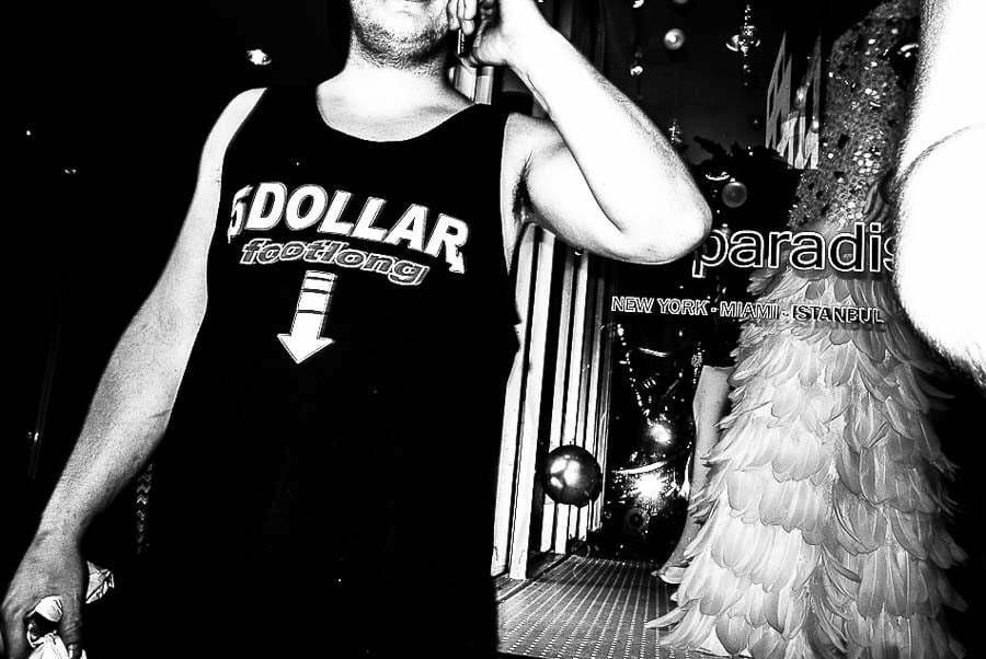Black and white street photo of a man on the phone wearing a tank top printed with the word DOLLAR