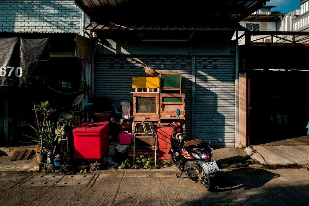 Color street photo of a shop front with a red cooler, potted plants and a parked motorbike in warm light