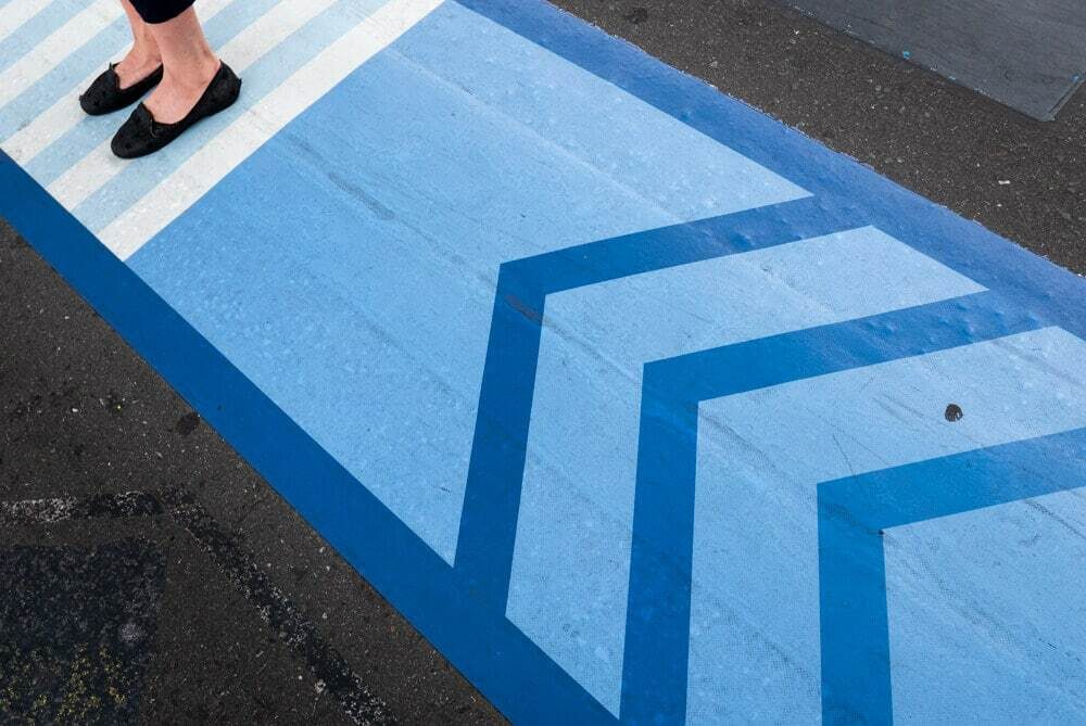 Blue striped crosswalk in Osaka seen from above with only a pair of feet visible at the top edge