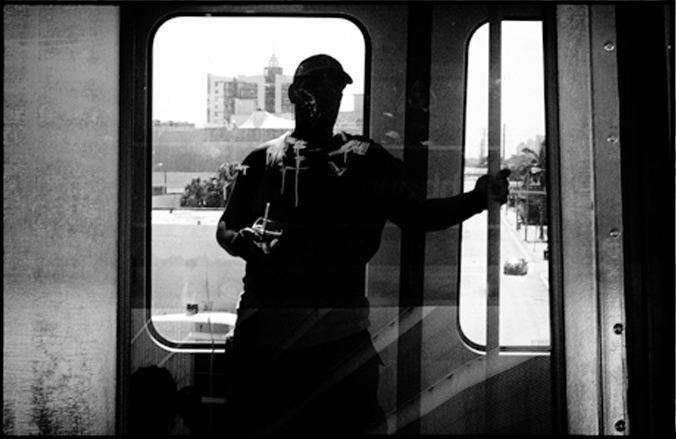 Black and white silhouette of a man standing in the open door of a train, backlit by a bright city