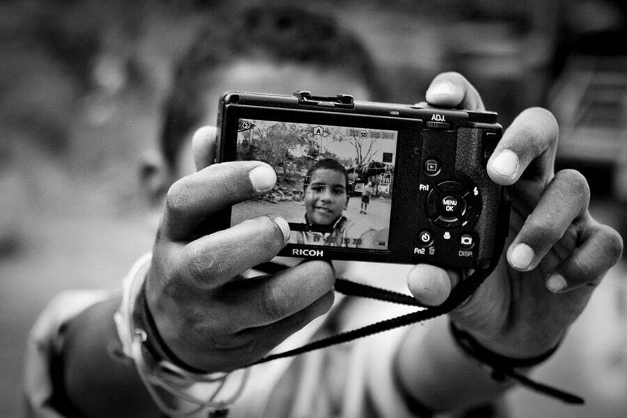 Boy holding up a Ricoh compact camera to show the photo on its LCD screen